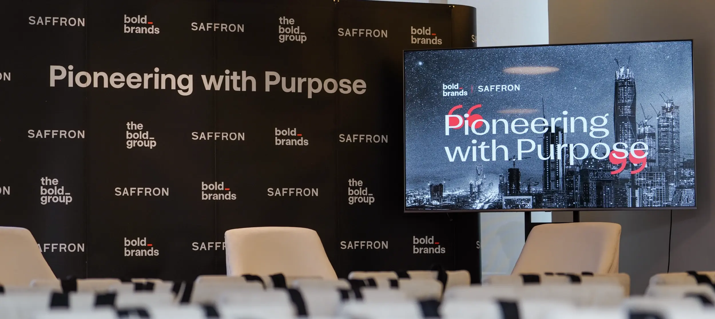 Stage setup for the 'Pioneering with Purpose' event in Riyadh, featuring a large screen with the event's logo and a backdrop displaying the Bold Brands and Saffron logos.